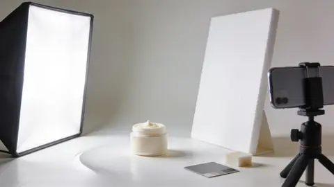 Предметная съёмка для фотокарточек маркетплейсов: косметический флакон на белом фоне, софтбокс, отражатель и смартфон на штативе