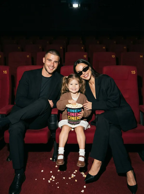 Ultra-realistic cinematic family lifestyle portrait of a mother, father, and daughter seated together in a modern cinema